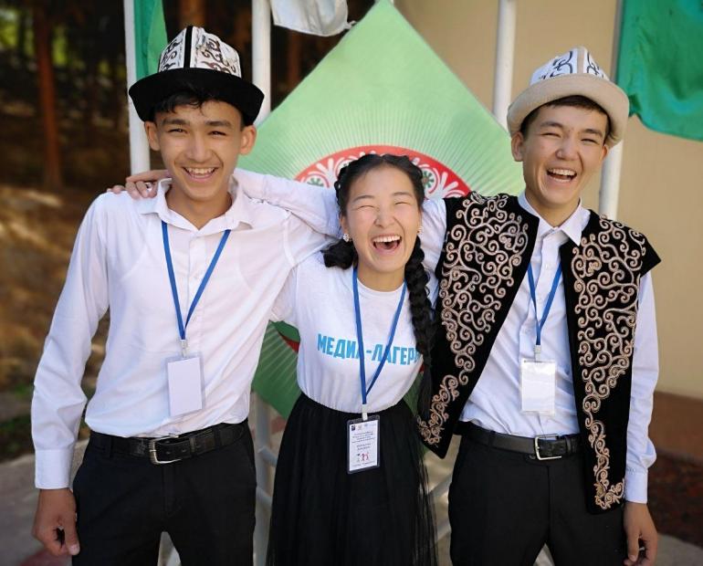 Three young people smile and laugh while standing side by side. 
