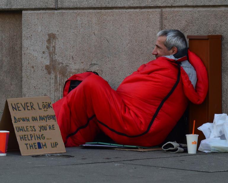 Homeless man carries sign reading: "never look down on anybody unless you're helping... them up."