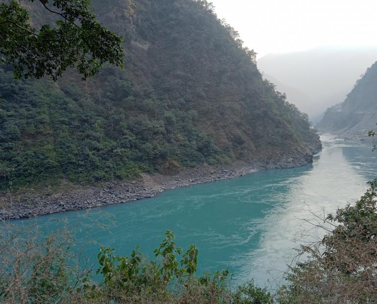 Image of clear water of river Ganga flowing along the base of the mountains.