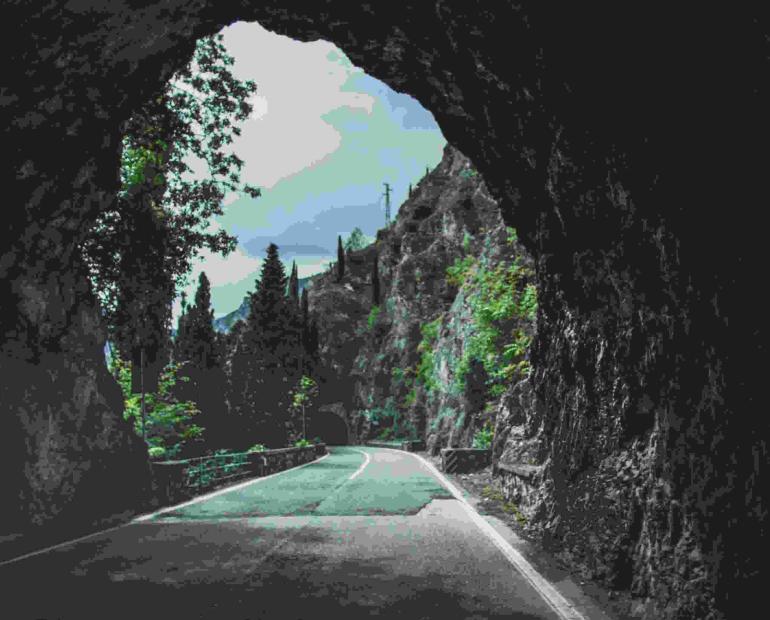 A mountain with trees and a light blue sky appear at the end of a rocky, dark tunnel.