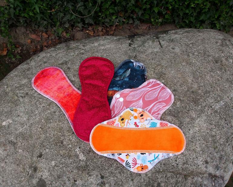 Five reusable fabric sanitary pads of different colors.
