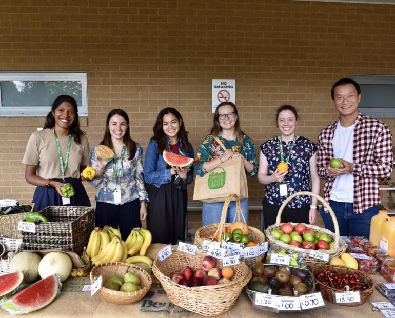 A group of young people pose in front a table with baskets of fruit.