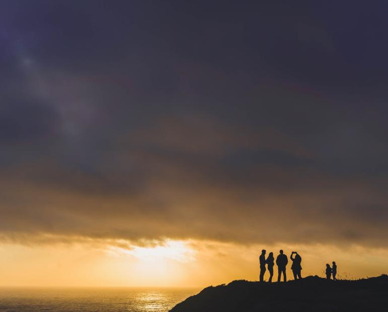 A photograph of 6 dark figures standing by the sunset 
