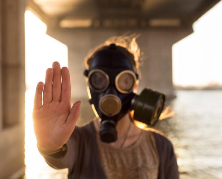 A person in a gas mask holds up their hand to the camera.