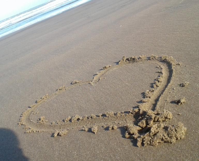 Un corazón dibujado en la arena, con el mar de fondo.