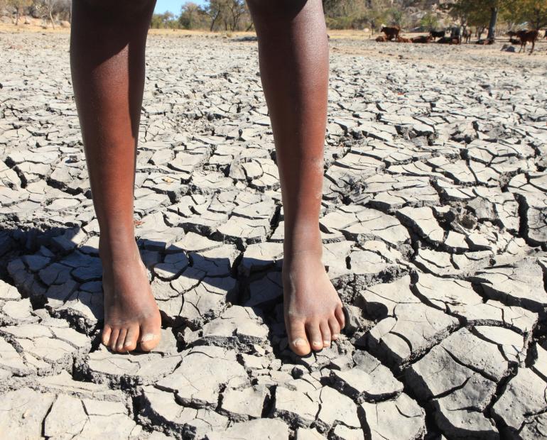 A close up of a child's legs standing on a dried mud.