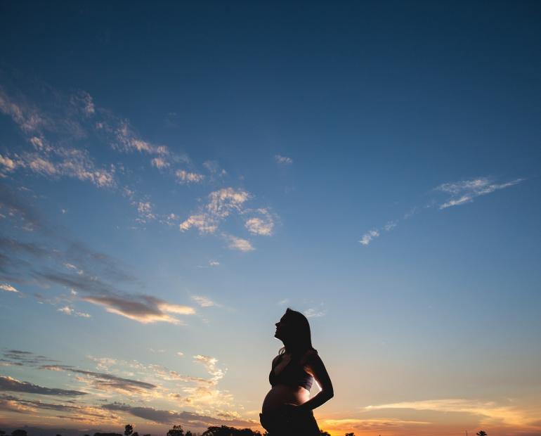 Imagen de una mujer embarazada mirando al cielo en el atardecer