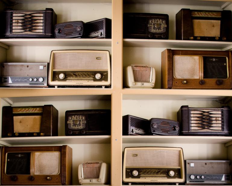 A shelf with lots of old radio sets displayed on it.