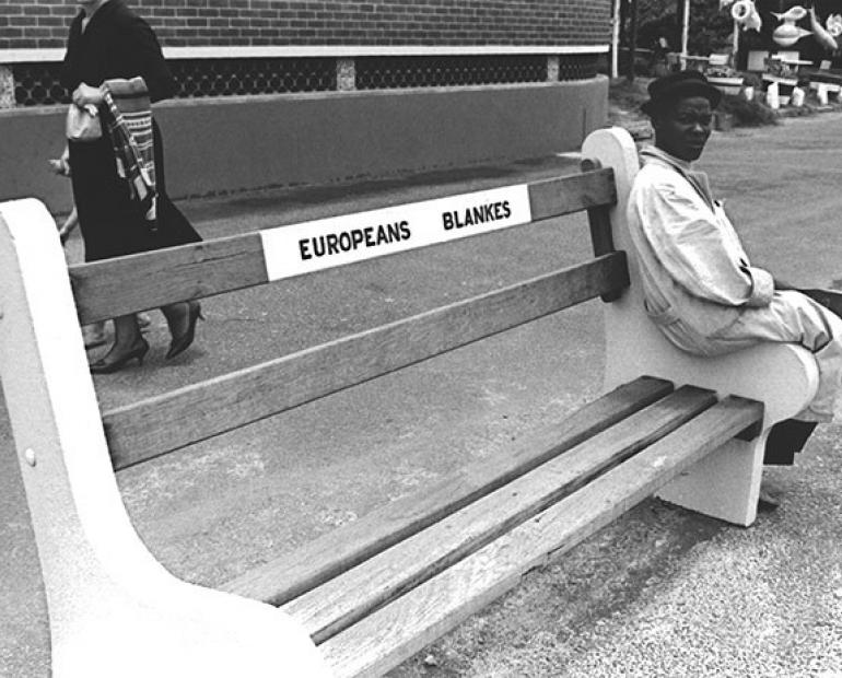 A black man sitting on a bench written Europeans only in Apartheid South Africa