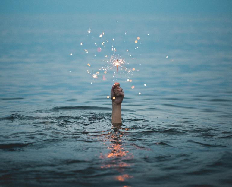 A hand holding a fireworks seen rising out of an ocean 