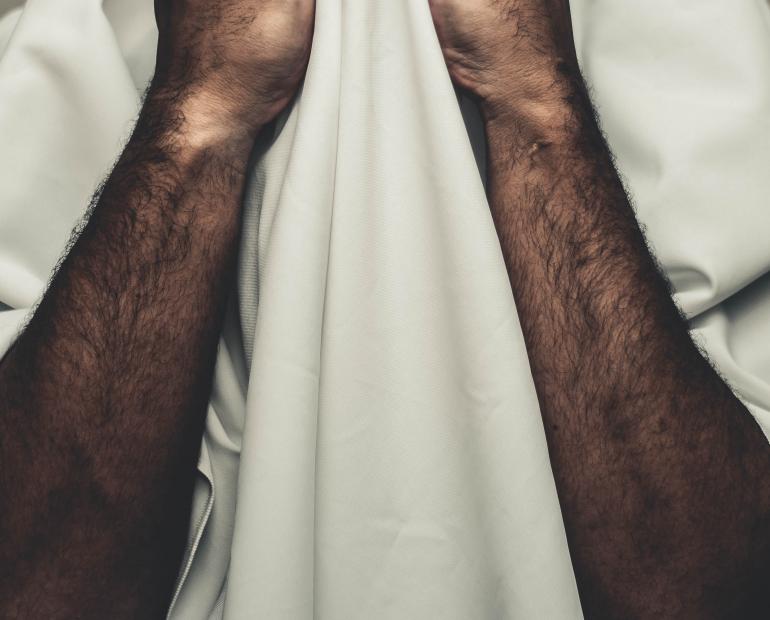 رجل يرتدي غطاء ابيض يستر به وجهه و يضع يديه على وجهه تشير الى الضغط و الاستياء و التستر و السكوت المجبر