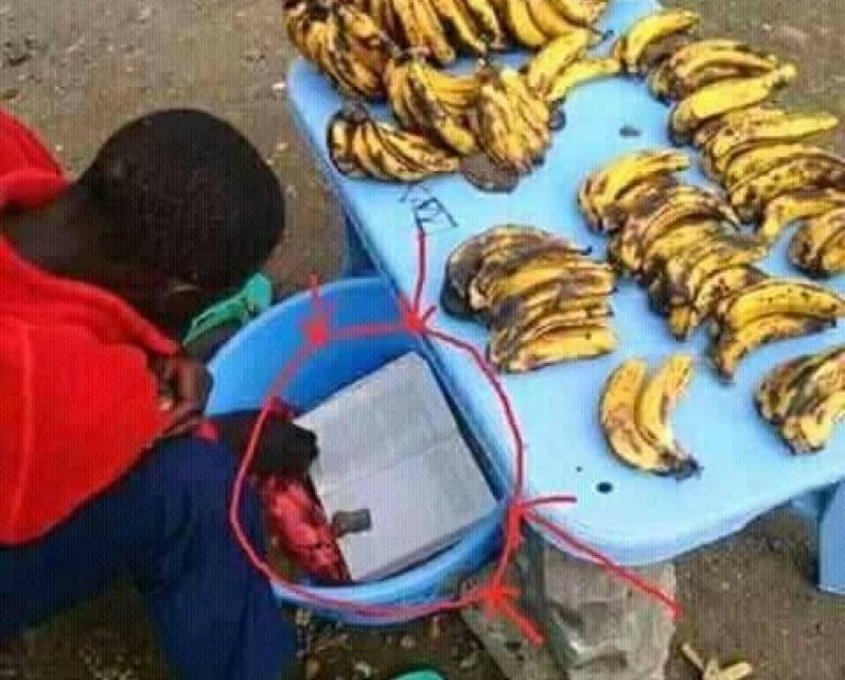 Child reading by the roadside as he sells banana.