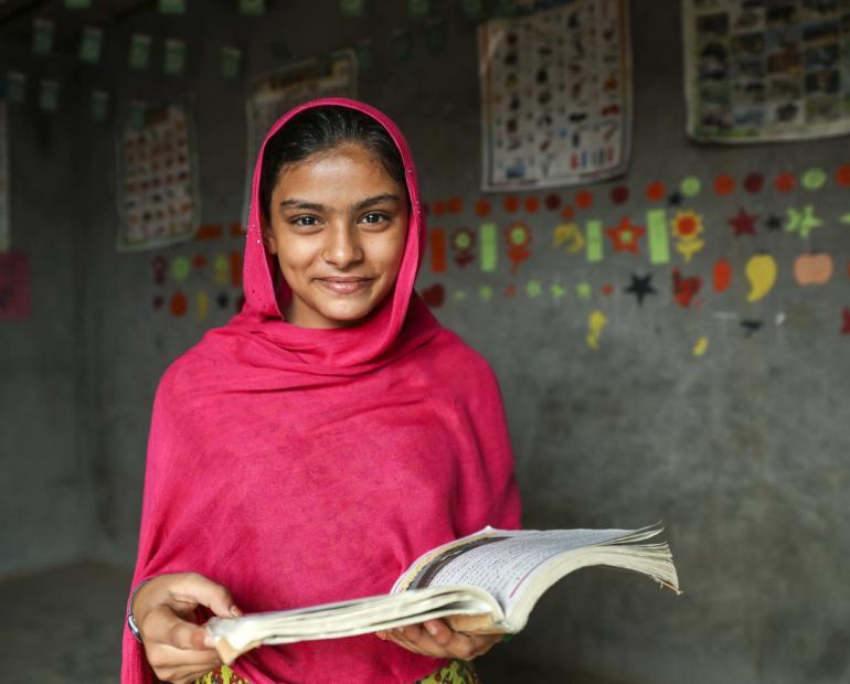 A young woman smiling and holding an open book. 