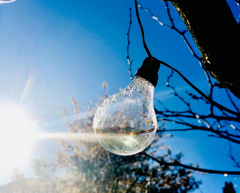 A lightbulb with the sun reflecting on it through the. The background features a blue sky.