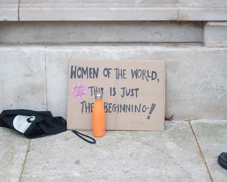 A cardboard sign that says "Women of the world, this is just the beginning"