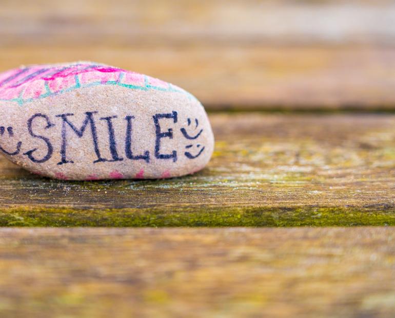 A rock with the word smile on it, surrounded by smileys