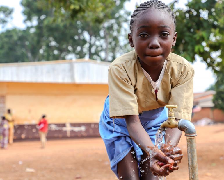 Un jeune fille qui lave ses mains dans la cour de l'école