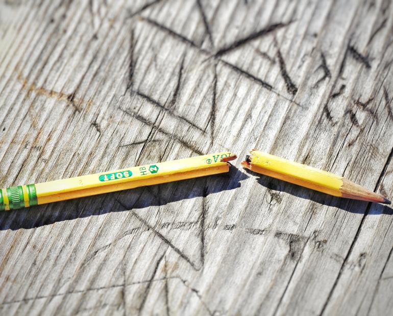 Un lápiz partido en dos puesto sobre una pieza de madera.