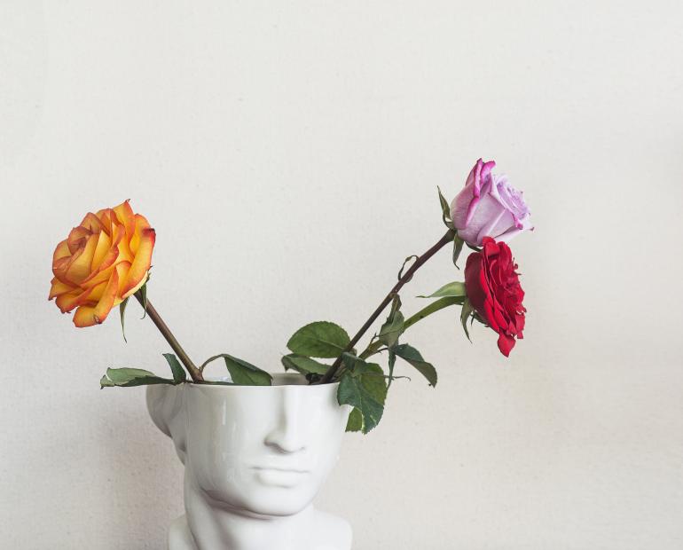 Three roses. One pink, one red, and one orange sit in an unusual vase.
