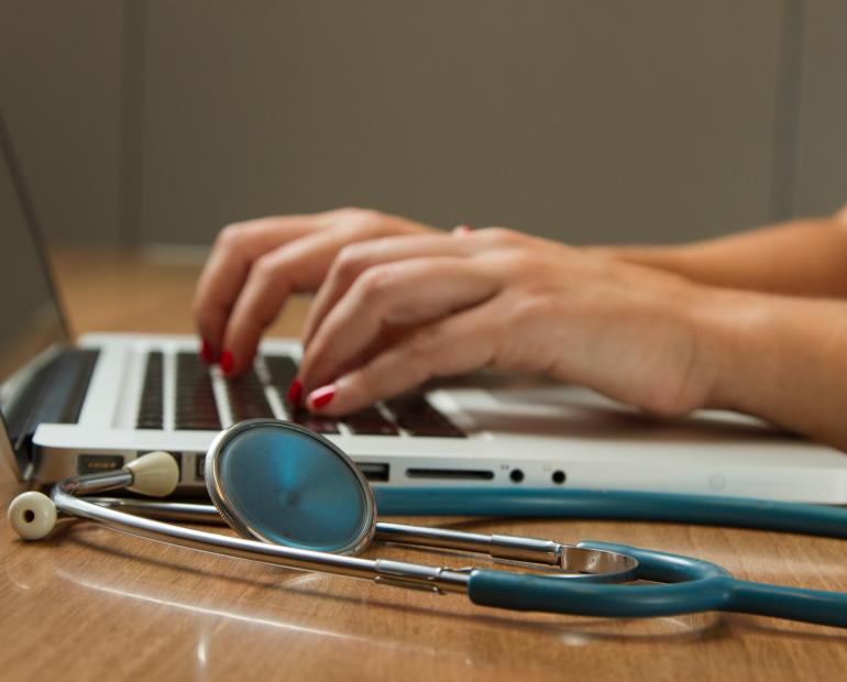 hands typing on laptop next to stethoscope 
