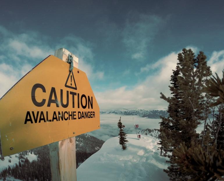 A sign board showing the word "caution" towards a snow-covered field.