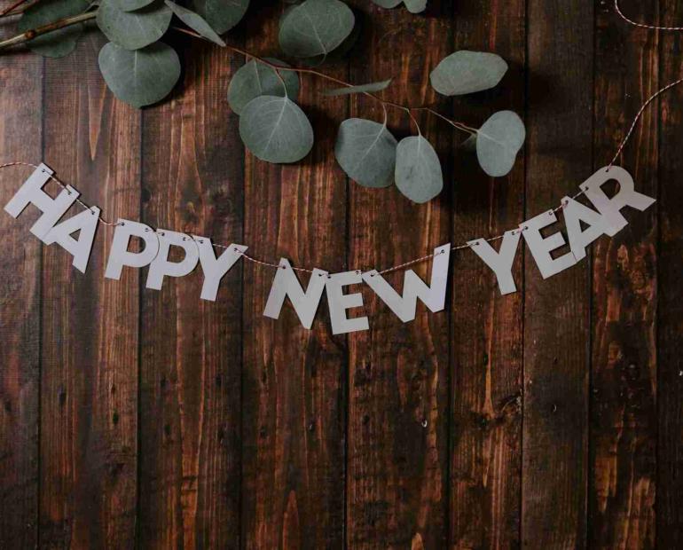 A sign says Happy New Year, over a wooden table, with eucalyptus leaves.