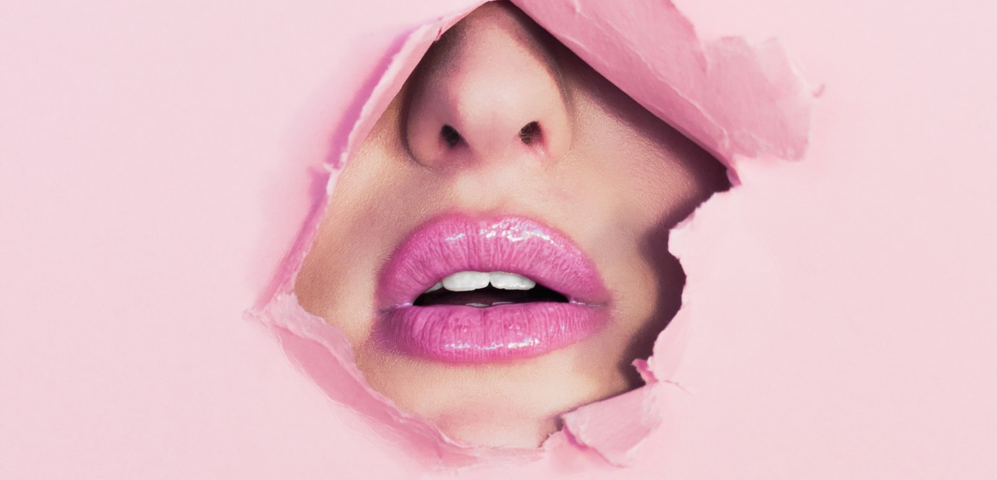 a womans lips and nose behind pink paper 