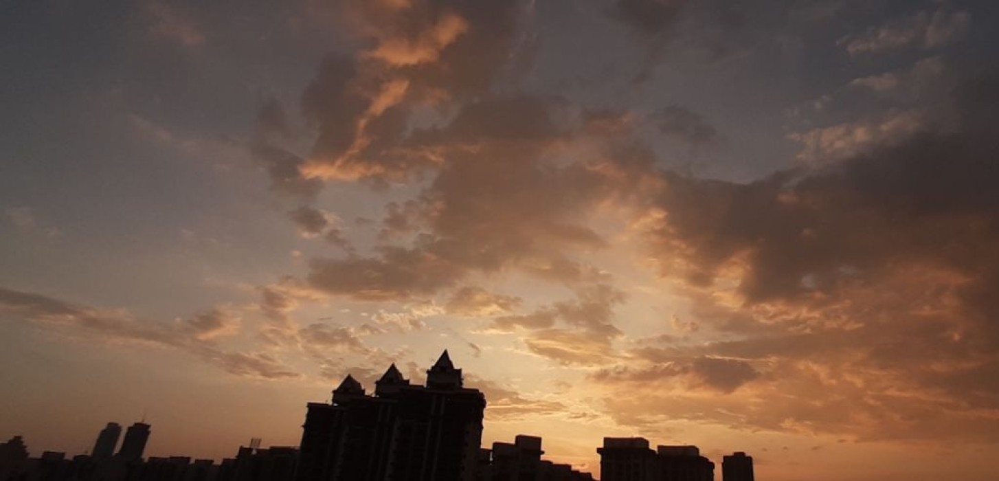 A beautiful sky, with splashes of cyan blue and light orange, accompanied by soft, scattered clouds. A silhouette of buildings marries into the scene.