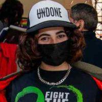 Nayor is wearing a white cap that says "Undone" with "Un" crossed out, and a black face mask, and appears to be smiling.