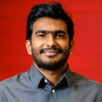 Akhil smiles at the camera, against a red backdrop.