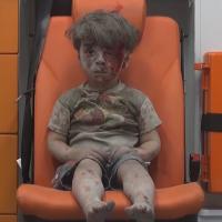 Omran sitting on an orange ambulance chair terrified with his face covered by dust and blood