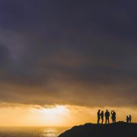 A photograph of 6 dark figures standing by the sunset 