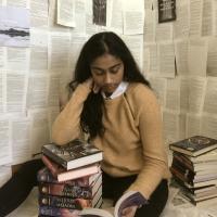 Girl in yellow shirt reading a book with book pages behind her