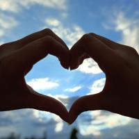 Upside hand down heart gesture with clouds and blue sky in the background