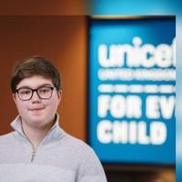 Smiling, sitting in front of a UNICEF UK sign.